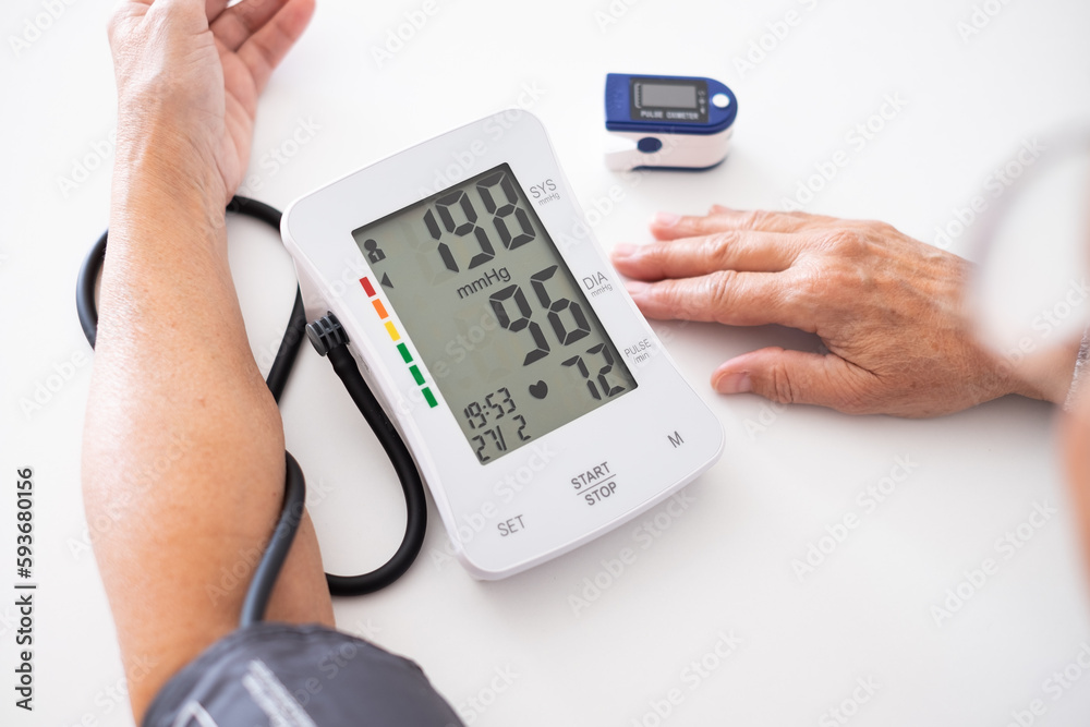 Elderly woman using medical device to measure blood pressure - senior woman suffering from hypertension sitting at home table taking care of her health Elderly woman using medical device to measure blood pressure - senior woman suffering from hypertension sitting at home table taking care of her health
