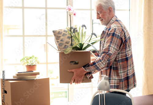 Hipster handsome senior man holding cardboard box posing in new house in moving day, concept of relocating, buying, renting house apartment