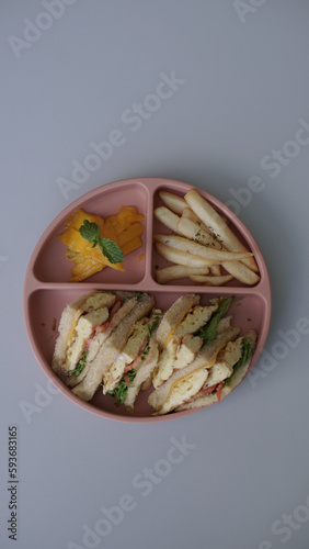 kids meal set, club sandwich with eggs fruits and vegetables, carrot tomato and cord, on food grade plate for kid, children or toddler, top view