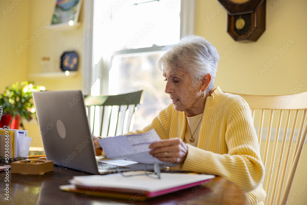 Senior Citizen at Home Paying invoice looking at laptop yellow room Senior Citizen at Home Paying invoice looking at laptop yellow room