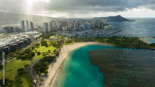 Aerial top view from above of Honolulu Hawaii cityscape with green park area and blue ocean at sunrise with lightrays and cloud shadows  photo