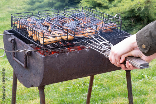 a man holds a grill with chicken over a barbecue with burning coals