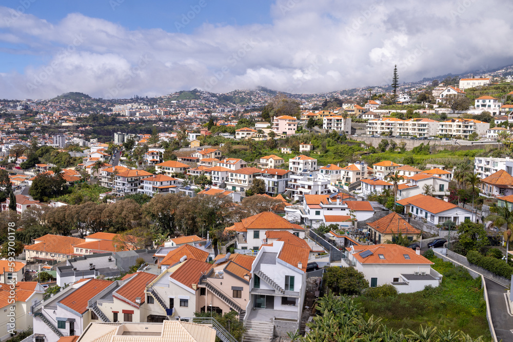 The beautiful town of Funchal in Madeira Island in Portugal showing typical Portuguese houses on a sunny summers day with clouds in the sky over the mountains.