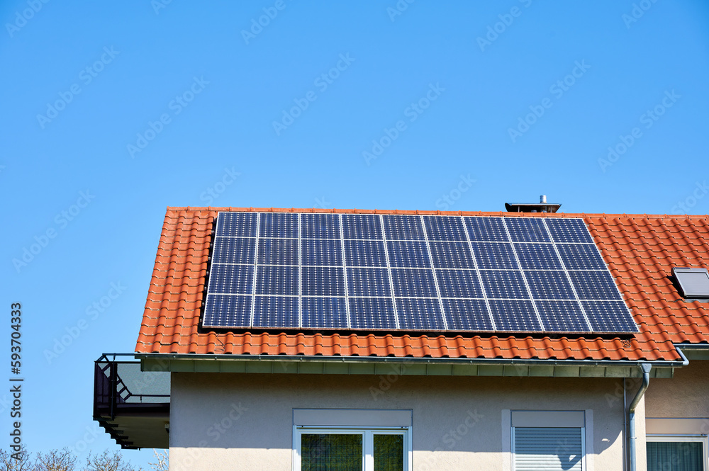 Fototapeta premium Solarzellen auf rotem Hausdach vor blauem Himmel