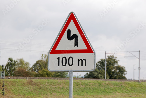 swiss traffic sign: double bend starting to the left. in 100 meters. cloudy during the day without people. drive slowly situation can be dangerous