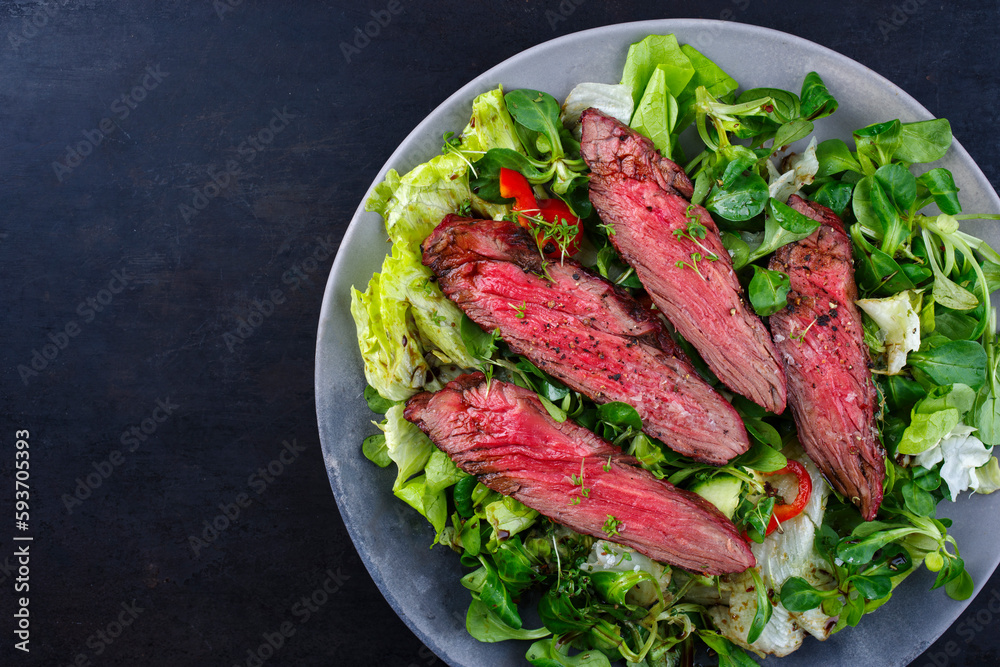 Traditional barbecue bavette beef steak slices with lambs salad and iceberg lettuce served as top view on a design plate with copy space left Traditional barbecue bavette beef steak slices with lambs salad and iceberg lettuce served as top view on a design plate with copy space left