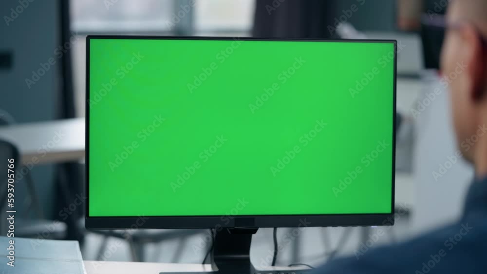 Young Man Working At Computer With Green Mock Up Screen in Office. Close Up Desktop Computer Monitor with Mock Up Green Screen Chroma Key Display Young Man Working At Computer With Green Mock Up Screen in Office. Close Up Desktop Computer Monitor with Mock Up Green Screen Chroma Key Display
