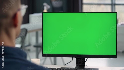 Young Man Working At Computer With Green Mock Up Screen in Office. Close Up Desktop Computer Monitor with Mock Up Green Screen Chroma Key Display
