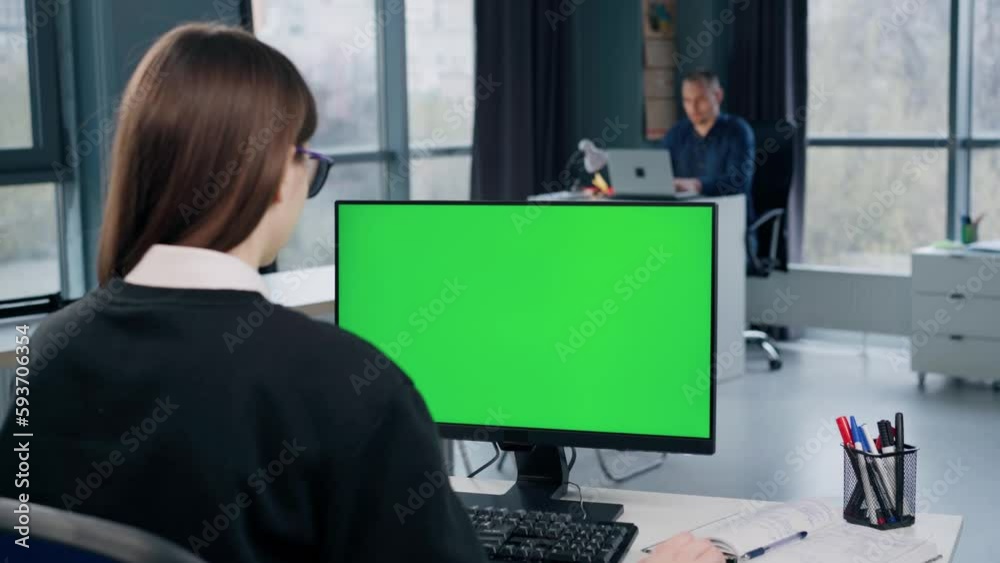 Young Woman Working At Computer With Green Mock Up Screen in Office. Girl Typing on Keyboard and Looking at PC Display