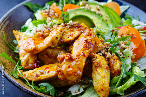 Traditional German iceberg and Italian arugula salad served with chicken, avocado and vegetables with spicy sweet and sour curry sauce as a creative and flavorful meal on a plate