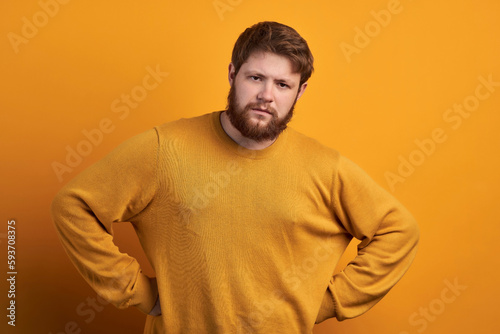 Beautiful bearded man with trendy haircut holding hands on waist, condemning looking at little kid,who trying to steal candy. photo