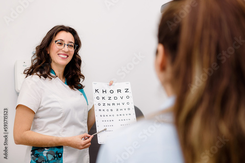 Oculist checking patients eyesight with eye chart photo