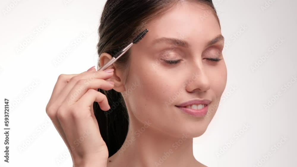 Smiling Beautiful female scrubs her eyelashes looking at the camera and smiling. Beauty concept. Close up view. Brunette caucasian woman paints her eyebrows with eyebrow brush. Smiling Beautiful female scrubs her eyelashes looking at the camera and smiling. Beauty concept. Close up view. Brunette caucasian woman paints her eyebrows with eyebrow brush.