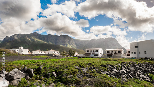 View of white houses situated on a mountain cliff against a mountain backdrop 