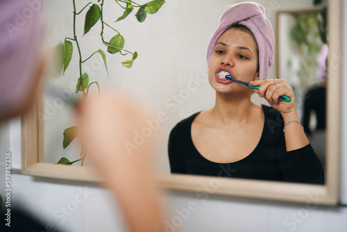 Young woman brushing teeth and looking in mirror photo