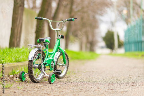 A green bicycle for children with additional wheels at road in park