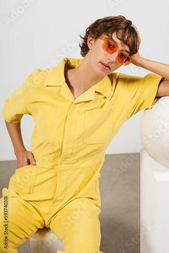 White girl with short hair and glasses wearing yellow jumpsuit