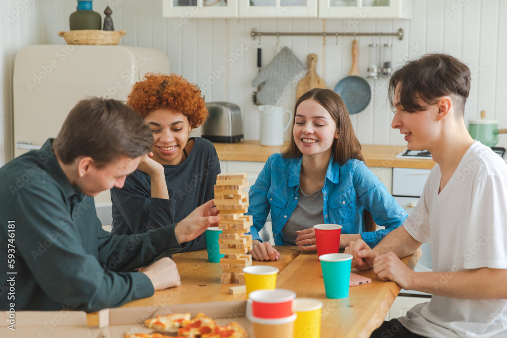 Home party. Friends spending time together playing in board game crash wooden tower at home. Happy diverse group having fun together indoor. Mixed race young buddies best friends enjoying weekend Home party. Friends spending time together playing in board game crash wooden tower at home. Happy diverse group having fun together indoor. Mixed race young buddies best friends enjoying weekend