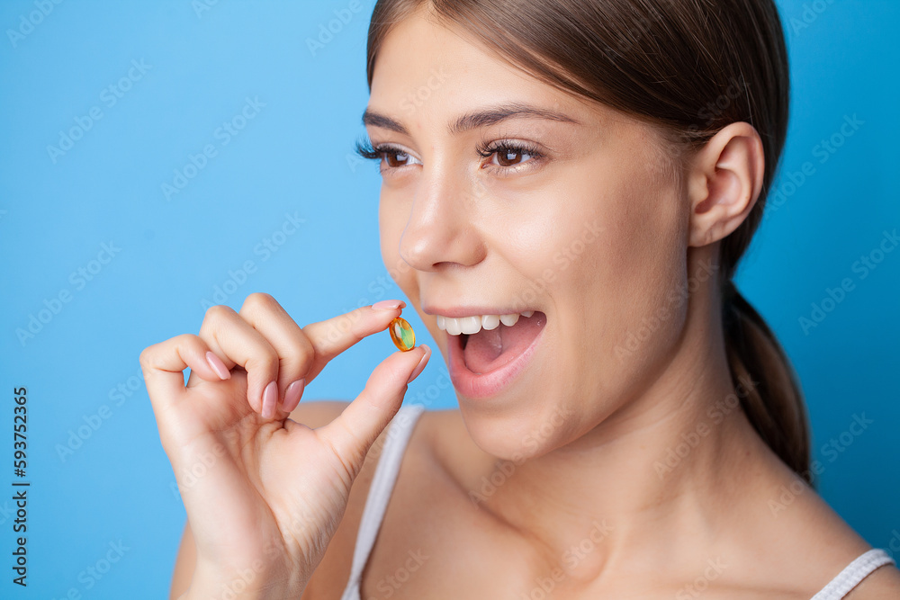 Woman holding omega-3 fish oil vitamin tablet on blue background Woman holding omega-3 fish oil vitamin tablet on blue background
