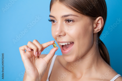 Woman holding omega-3 fish oil vitamin tablet on blue background