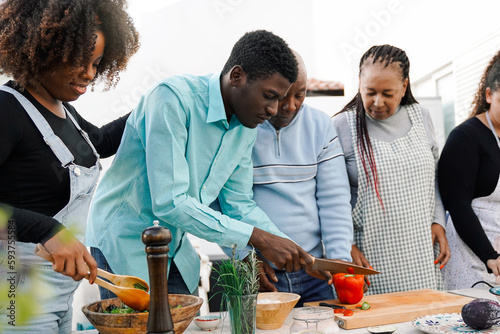 Outdoor kitchen: African family cooking vegetarian food at home patio - Father, mother, daughter, brother making healthy food dinner - Soft focus on right daughter face