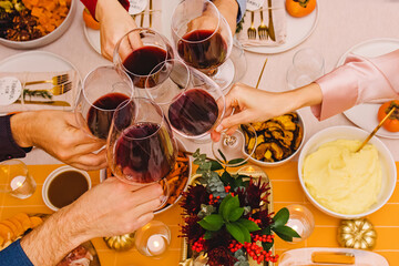Hands clinking with a glasses filled with red wine sitting at the Thanksgiving dinner table