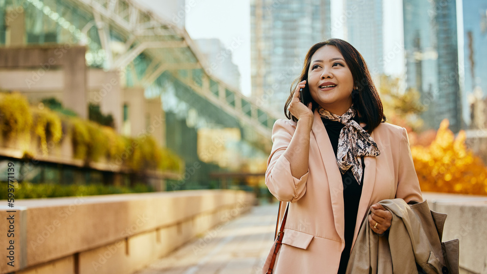 Fototapeta premium Asian businesswoman communicating on cell phone on city street.