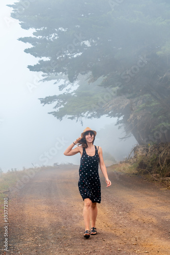 Tourist woman with hat walking through the foggy path towards the juniper forest in El Hierro. Canary Islands