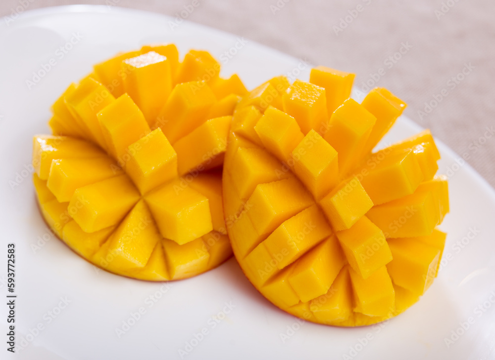 on table covered with tablecloth- two halves of ripe orange mango cut into cubes lie on white round plate.Isolated