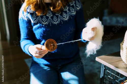 Woman in bright blue sweater in her living room and hand spinning yarn photo