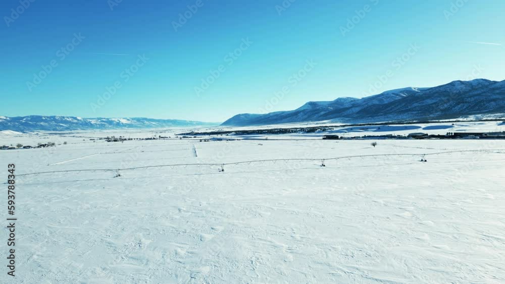 Aerial-Pulling back over snowy fields with distant snow covered mountains and sprinkler line idled for the winter Aerial-Pulling back over snowy fields with distant snow covered mountains and sprinkler line idled for the winter