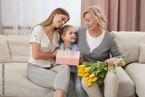 Little girl congratulating her mom and granny with flowers and gift at home. Happy Mother's Day