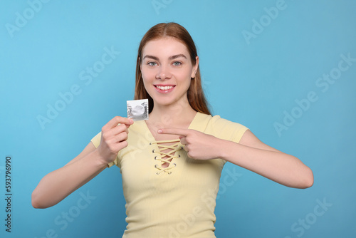 Woman holding condom on turquoise background. Safe sex