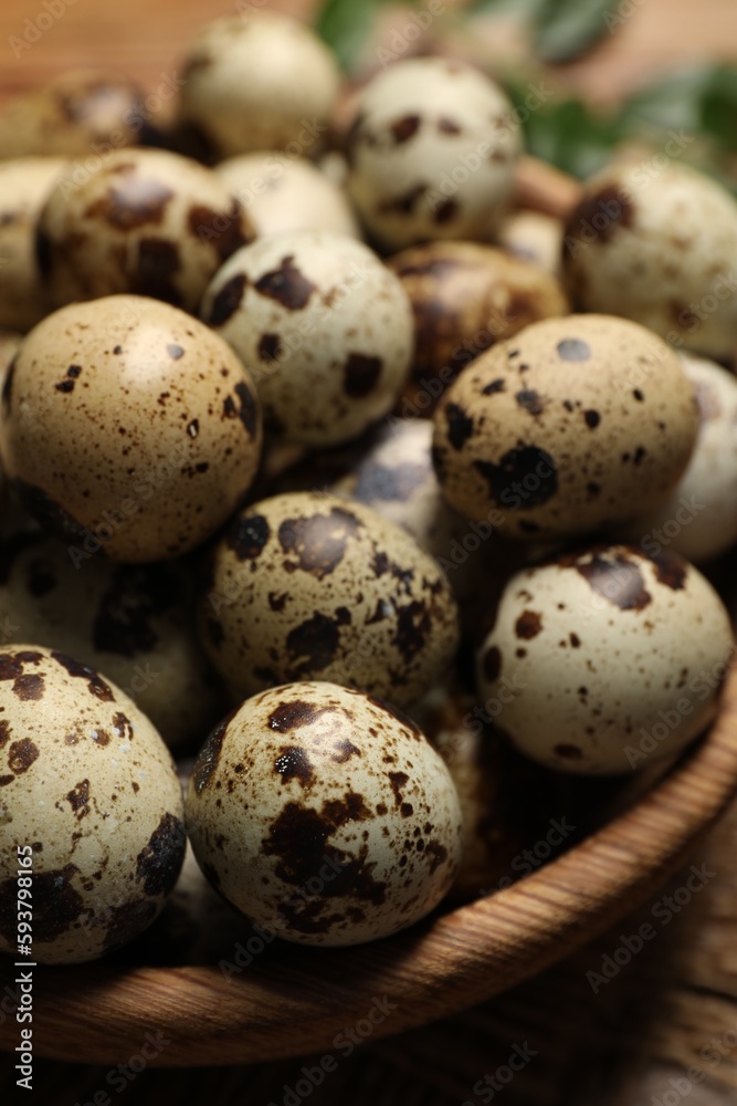 Wooden bowl with quail eggs on table, closeup