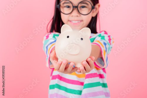 Little Asian girl saving money in a piggy bank, learning about saving, Kid save money for future education. Money, finances, insurance, and people concept