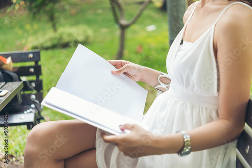 Asian woman holding book reading magazine at green park in natural garden. Young woman relaxation read open book self study. University women smiling with happiness learning. Women sit in green park