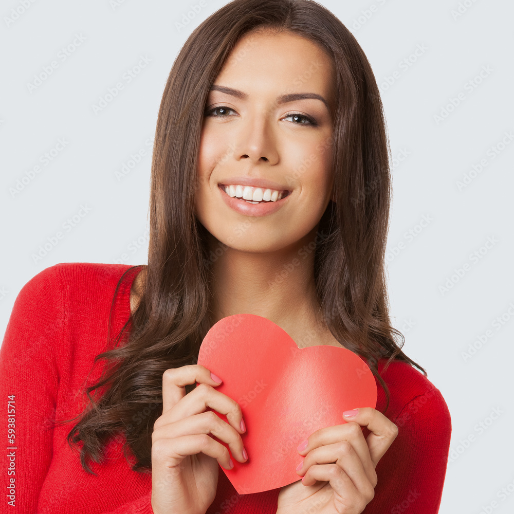 Square image of happy smiling asian caucasian woman in red casual cloth wear, sweater, isolated on light grey gray background. Brunette girl showing handmade heart paper symbol. Square image of happy smiling asian caucasian woman in red casual cloth wear, sweater, isolated on light grey gray background. Brunette girl showing handmade heart paper symbol.