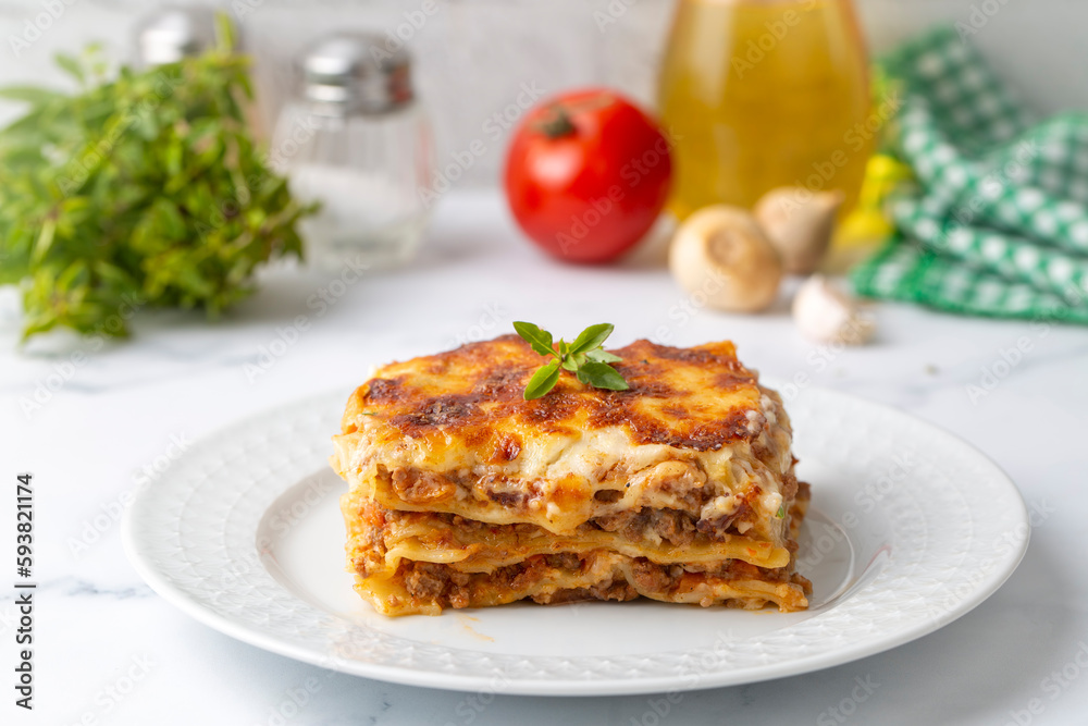 Portion of ground beef lasagna topped with melted cheese and garnished with fresh parsley served on a plate in close view for a menu Portion of ground beef lasagna topped with melted cheese and garnished with fresh parsley served on a plate in close view for a menu