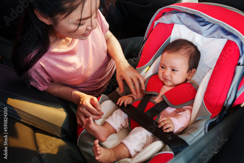 mother consoling newborn baby crying while putting and fasten seat belts on car seat