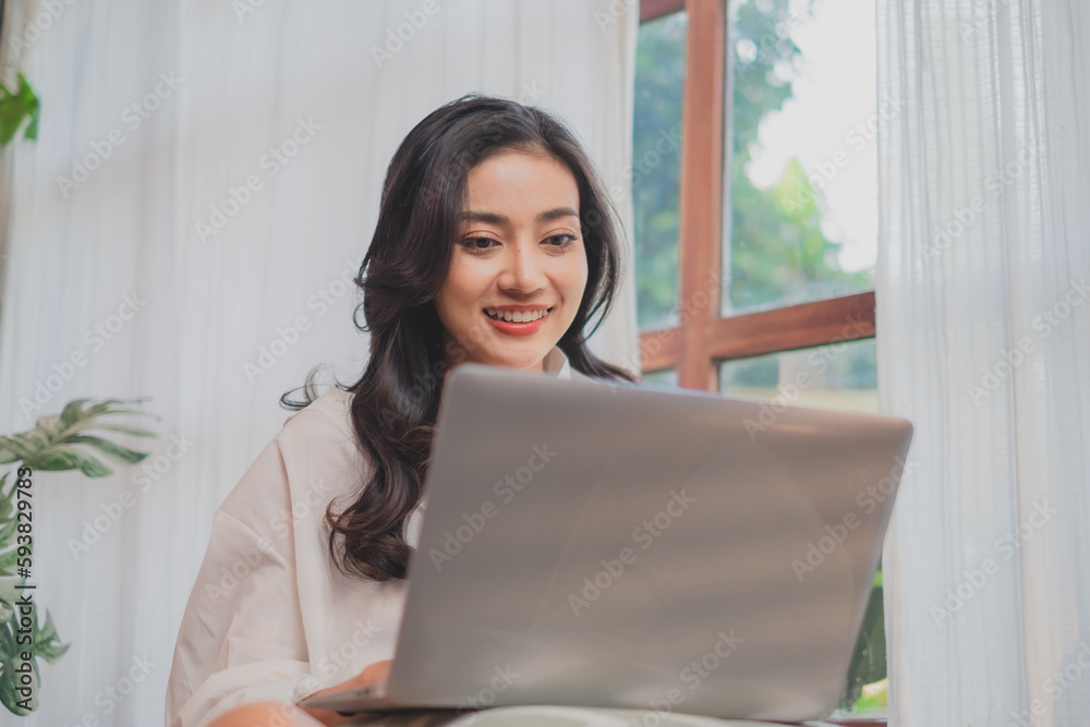 Smiling Asian woman sit relax and using laptop browsing, searching or working wireless internet, happy young woman freelancer work on computer typing texting from home or vacation. online shopping. Smiling Asian woman sit relax and using laptop browsing, searching or working wireless internet, happy young woman freelancer work on computer typing texting from home or vacation. online shopping.