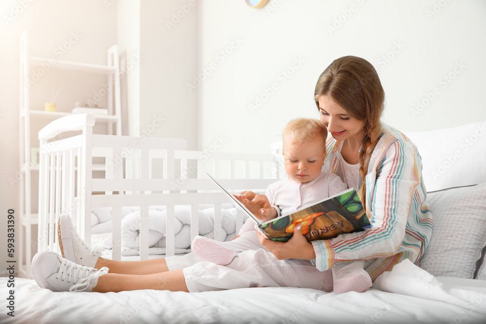 Young mother reading book to her cute little baby on bed - obrazy, fototapety, plakaty 