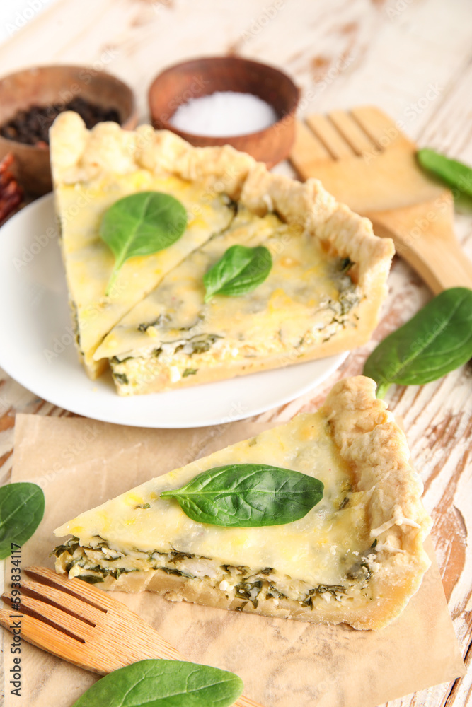 Plate with pieces of delicious quiche and spices on white wooden background Plate with pieces of delicious quiche and spices on white wooden background