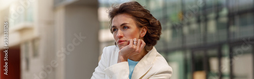 Focused woman in white suit standing near business centre. Blurred background
