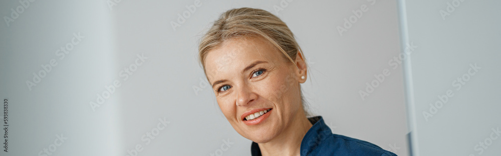 Smiling doctor with clipboard standing near reception in clinic hall and looking camera Smiling doctor with clipboard standing near reception in clinic hall and looking camera