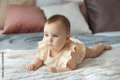 Portrait of newborn child relaxing in bed. Cute infant baby girl 6 month old.