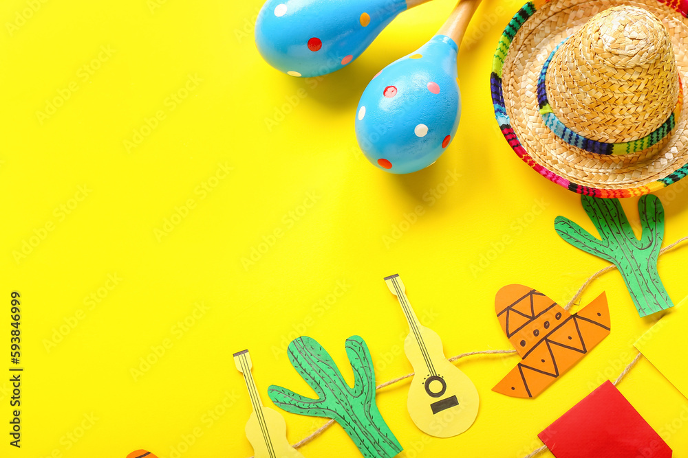 Mexican maracas with sombrero hat and paper garland on yellow background, closeup