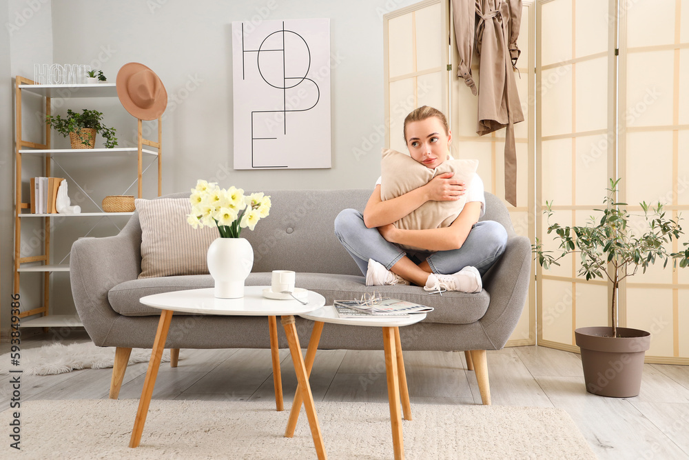 Thoughtful young woman with pillow sitting on sofa at home Thoughtful young woman with pillow sitting on sofa at home