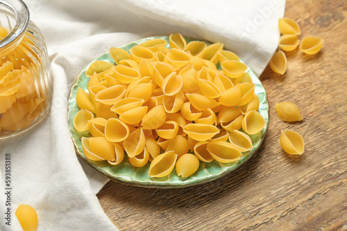 Plate with raw conchiglie pasta on wooden background photo