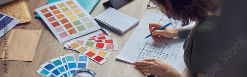 Close up shot of working process of interior designer making notes on a blueprint, selecting color samples, sitting at the table in her office photo