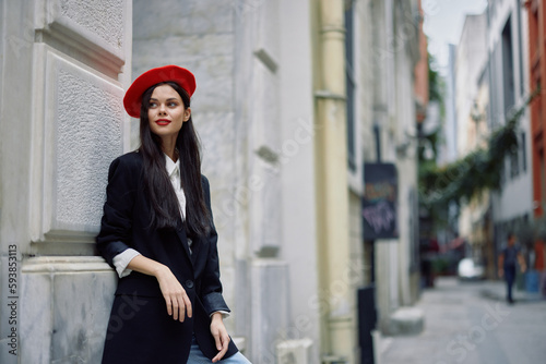 Woman standing near a wall in the city wearing a stylish jacket and red beret with red lips, travel and leisure, French style of dress, spring.